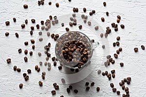 A Cup filled with coffee beans. Coffee beans are scattered on the white surface of the table
