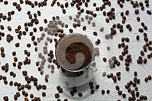 A Cup filled with coffee beans. Coffee beans are scattered on the white surface of the table