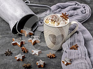 A cup filled with whipped cream and cocoa powder is decorated with star anise, coconut stars, a gray scarf and a vintage vase