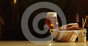 A cup of foamy beer with a pretzel and a light snack on a wooden table.