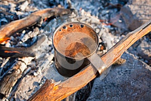 Cup of fragrant coffee with foam on a campfire, tourist morning