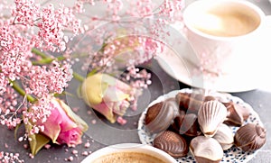 A cup of fragrant coffee in the morning and a bouquet of pink flowers. Chocolate sweets in the form of cockleshells. Shells on the