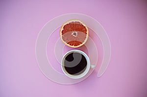 A cup of coffee on and a half of grapefruit on pink background.