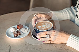 A cup of fresh cappuccino coffee in the hands of a woman on a fashionable background of a white marble table, next to a