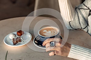 A cup of fresh cappuccino coffee in the hands of a woman on a fashionable background of a white marble table, next to a