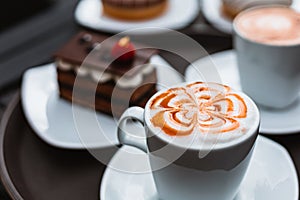 Cup of a fresh caramel latte with whipped cream on the table and chocolate cake