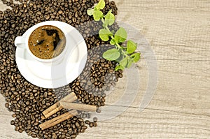 Cup of fresh coffee, coffee beans, cinnamon and mint tea flowers