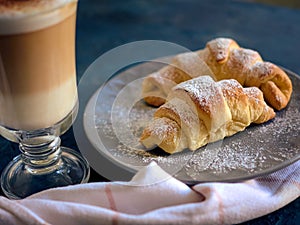 A cup of fresh coffee with croissants on a dark blue background, selective focus