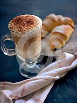 A cup of fresh coffee with croissants on a dark blue background, selective focus