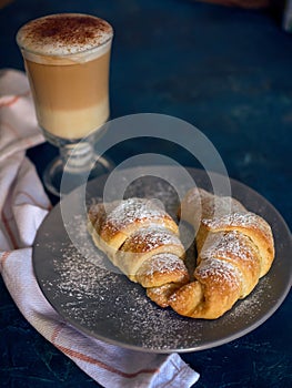 A cup of fresh coffee with croissants on a dark blue background, selective focus