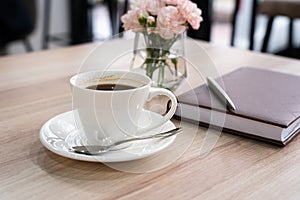 Cup of fresh coffee with notebook and pen on the table. Business meeting in a cafe. Close-up. Selective focus