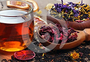 Cup of fresh tea and different varieties of tea leaves. blended tea with flower petals, hibiscus in a wooden spoon and dried citru