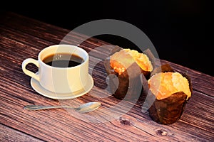 A cup of freshly brewed black coffee and two muffins on a wooden table