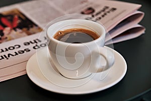 Cup of freshly brewed coffee on the table with a newspaper