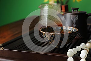 Cup with freshly brewed pu-erh tea and prayer beads on wooden tray, closeup. Space for text