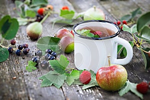 Cup of fruit tea with apples, pears, raspberries and black currant berries on wooden table outdoors.