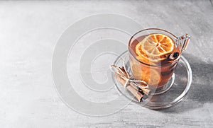 Cup of fruit tea with dry orange and cinnamon on gray background. Glass teacup