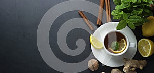 Cup of ginger tea with lemons and mint leaves on dark background. Banner, cold and autumn time