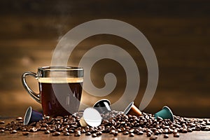 Cup glass of coffee with smoke and coffee beans and coffee capsule on old wooden background photo