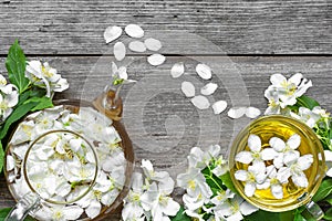 Cup of green herbal tea with jasmine flowers and teapot over rustic wooden background