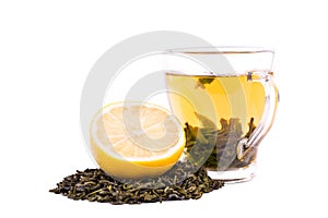 A cup of green tea isolated on a white background. A sweet tea cup next to a cut lemon and a heap of natural green tea leaves.