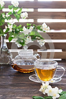 Cup of green tea with jasmine flowers and tea pot on wooden background. Copy space