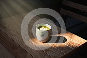 A cup of green tea matcha latte on wooden table at cafe. Healthy food concept. Sun rays. Side view. Close-up