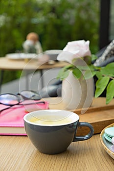 A cup of green tea on a wooden table with a notebook and glasses on a green background