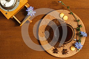 A Cup of ground chicory root coffee on a wooden stand decorated with chicory flowers and a vintage coffee grinder. Overhead with photo