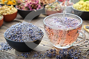Cup of healthy lavender tea and dry lavender flowers. Healthy lavender tea poured into glass cup. Bowls of dry medicinal herbs. photo