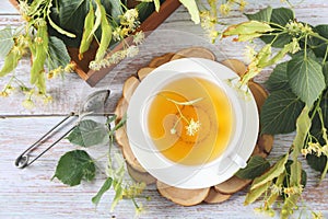 Cup of herbal linden tea with linden flowers on light background