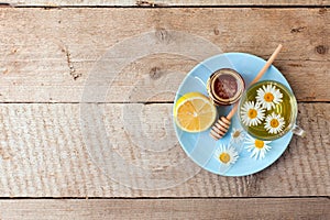 Cup of herbal tea with chamomile flowers, honey and lemon on a wooden table, rustic seasonal tea party