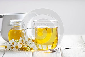 Cup of herbal tea with chamomile flowers and honey on the white wooden background. Natural organic alternative medicine