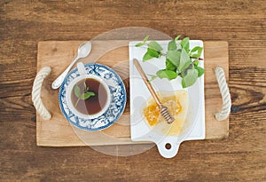 Cup of herbal tea with fresh mint and honey on wooden tray over rustic background. Top view.