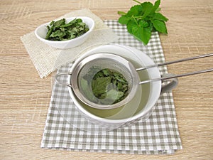 A cup of herbal tea with goutweed in a tea strainer