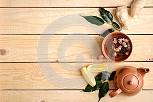 Cup of herbal tea, teapot, lemon, plants leaves and ginger root on rustic wooden background, view from above, flat lay composition