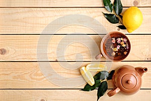 Cup of herbal tea, teapot, lemon and plants leaves on rustic wooden background, view from above, flat lay composition with copy