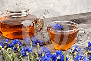 Cup of herbal tea, transparent teapot and blue cornflowers flowers on wood background. Top view Flat lay