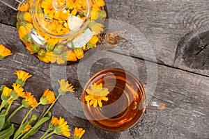 Cup of herbal tea and transparent teapot and marigold flowers on wood background. Calendula Tea Benefits Your Health