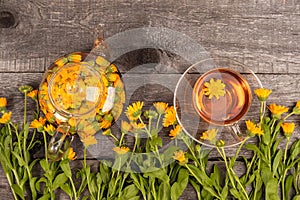 Cup of herbal tea and transparent teapot and marigold flowers on wood background. Calendula Tea Benefits Your Health