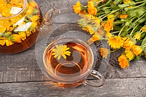 Cup of herbal tea and transparent teapot and marigold flowers on wood background. Calendula Tea Benefits Your Health