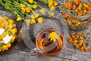 Cup of herbal tea, transparent teapot and marigold flowers on wood background. Calendula Tea Benefits Your Health concept. Front