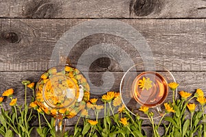 Cup of herbal tea and transparent teapot and marigold flowers on wood background. Calendula Tea Benefits Your Health concept. Top