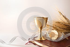 Cup and hosts on bible with ribbon and wheat ears