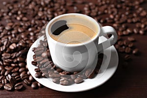 Cup of hot aromatic coffee and roasted beans on wooden table, closeup