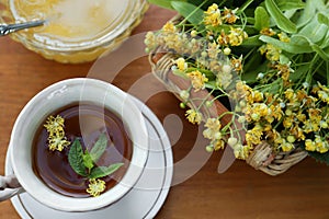 Cup of hot aromatic herbal tea, honey and linden blossoms on wooden table, above view