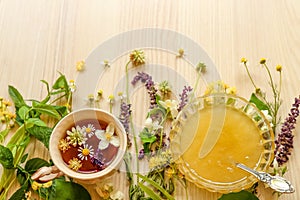 Cup of hot aromatic tea, honey and different fresh herbs on white wooden table, above view