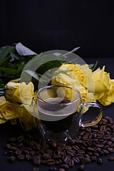 Cup of hot black coffee on coffee beans with yellow roses