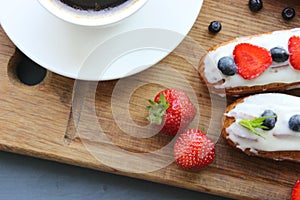A Cup of hot black coffee and delicious eclairs with strawberries and blueberries on a wooden cutting Boar