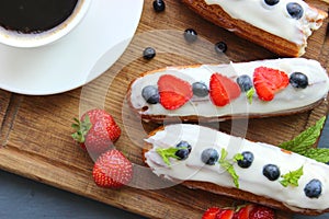 A Cup of hot black coffee and delicious eclairs with strawberries and blueberries on a wooden cutting Boar